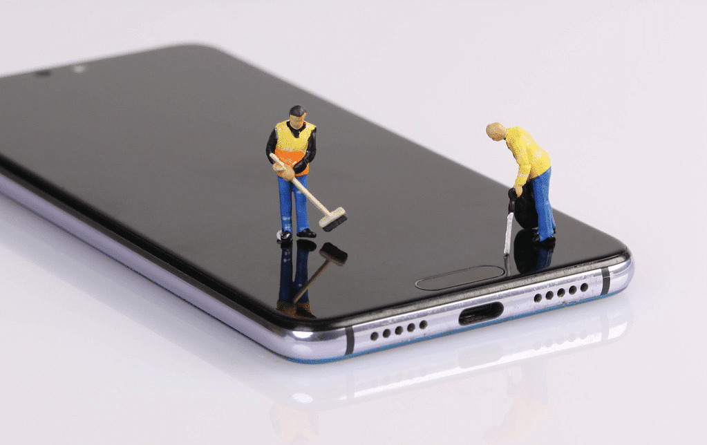 Two small figures of workers with brooms and leaf blowers posed to be "cleaning" a cell phone.