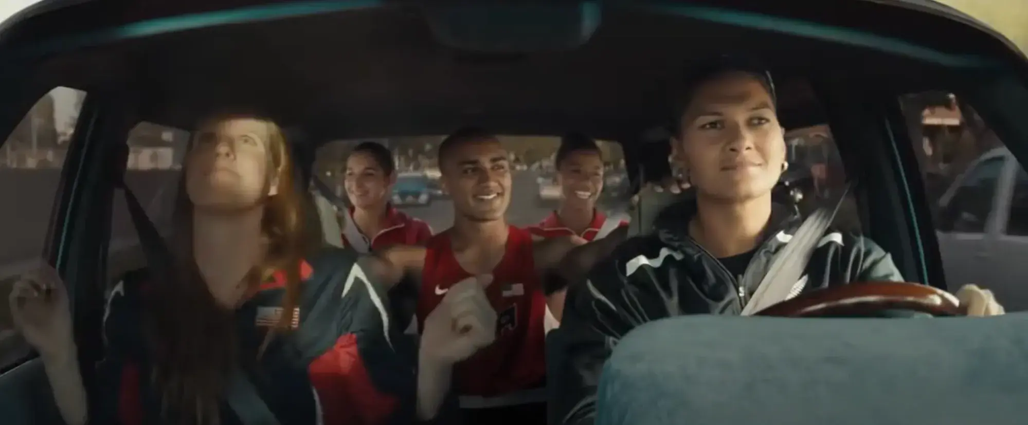 Screencap from ad. Five Olympic athletes in a car on a road trip.