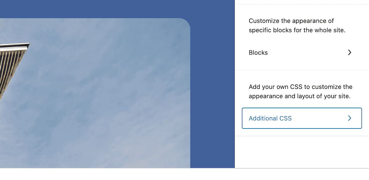 A partial view of the WordPress Site Editor showing links to the Blocks and Additional CSS settings. The left-hand side of the screen displays a partial view of a building against a blue sky.